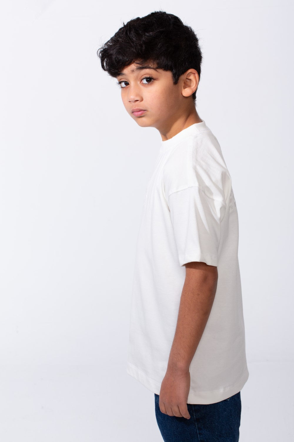 A boy wearing an oversized white crew neck t-shirt with typography embroidery on the back.